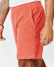 Vibrant coral terry cloth Mens Tristan Short with a relaxed fit, featuring an all-over embossed diamond pattern and a small embroidered Psycho Bunny skull logo on the left thigh. (3)