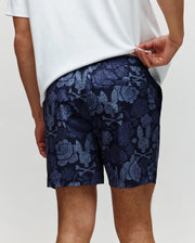 A person in a white shirt lifts it to reveal the stylish Psycho Bunny MENS ROWEN SWIM TRUNK - MB1000023, navy blue with a light blue floral pattern, shown from the back.