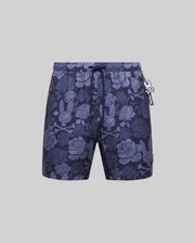 The Psycho Bunny MENS ROWEN SWIM TRUNK (MB1000023) features dark blue floral designs with light blue skulls, a drawstring waistband, and a small rabbit-shaped keychain on the left, shown against a plain gray background.