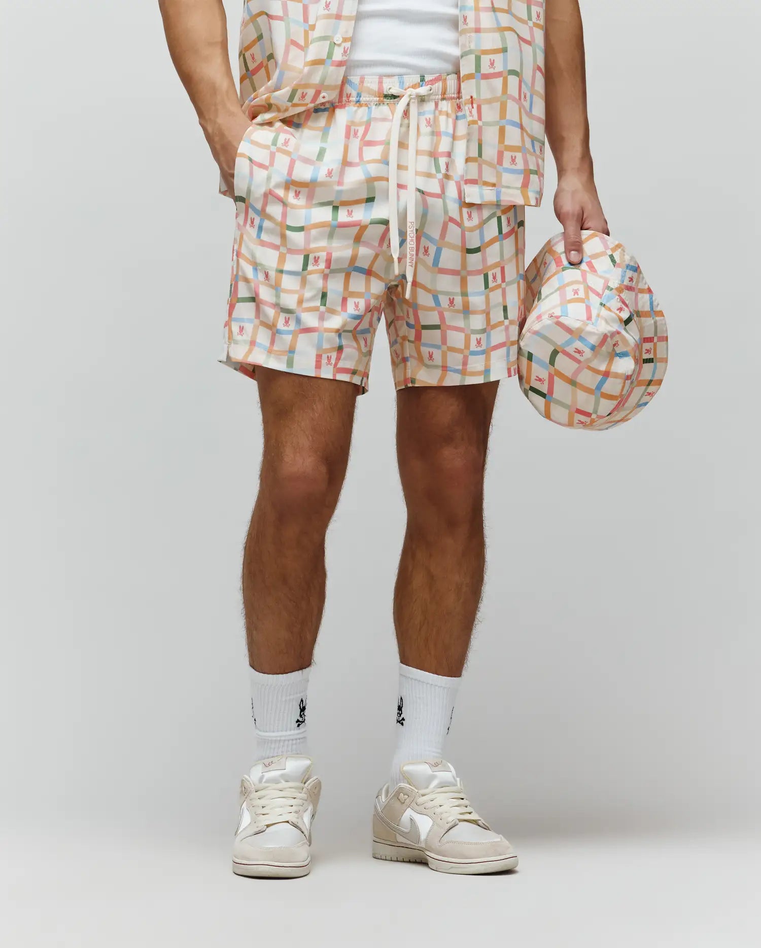 Mens Atlas Swim Trunk in cream with a vibrant multicolor plaid pattern, featuring small repeated Psycho Bunny skull logos and PSYCHO BUNNY text on the drawstring. Relaxed fit, smooth quick-dry fabric.