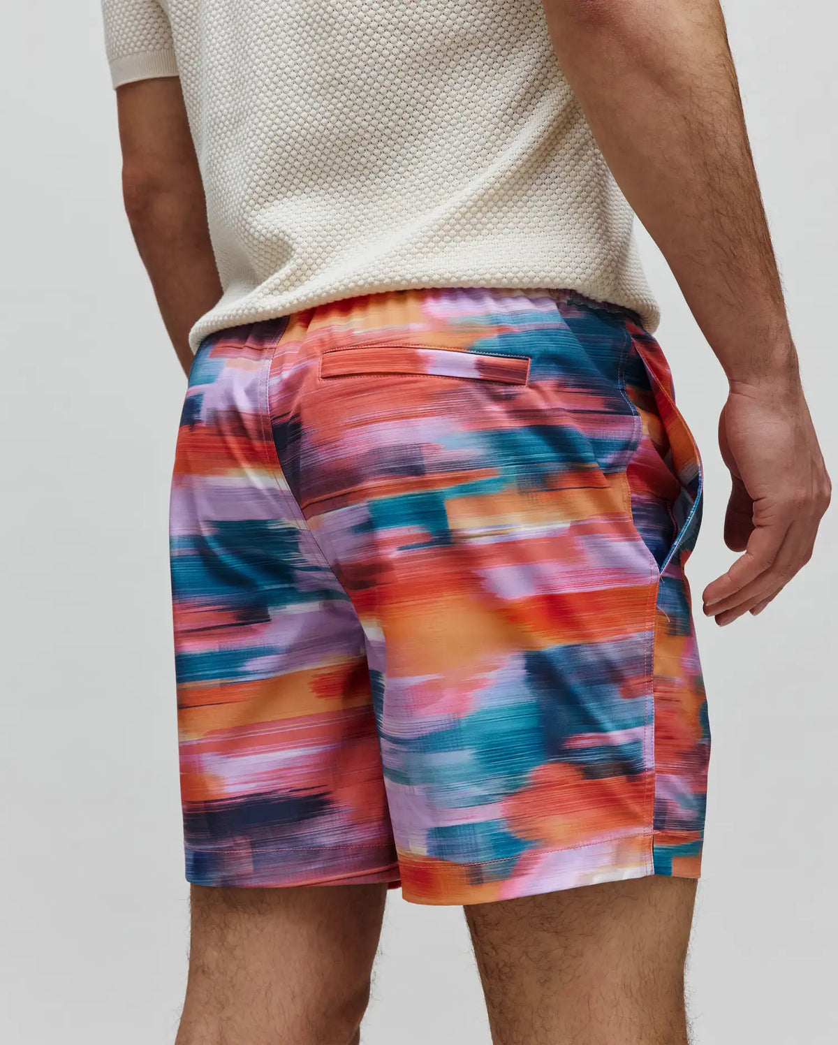 Mens Raphael Swim Trunk featuring a vibrant abstract brushstroke pattern in orange, red, pink, purple, blue, and teal. This relaxed-fit trunk has smooth quick-dry fabric and a back flap pocket.