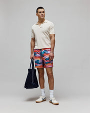 Cream pique knit polo with open collar and subtle chest Psycho Bunny logo, paired with Mens Raphael Swim Trunk featuring a vibrant abstract multi-color print and small leg bunny skull logo.