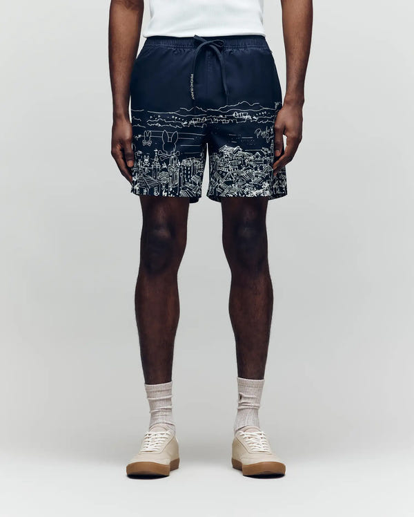 A person wears a white sleeveless shirt, Psycho Bunny MENS NAXOS SWIM TRUNK - MB1000005 with a white cityscape print, beige socks, and light beige sneakers against a plain background. The image is torso-cropped for an all-day comfort look.