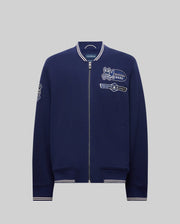 The Psycho Bunny MENS DESMOND PIQUE KNIT BOMBER - MO1100018 is a navy bomber with white trim, varsity-style details, and embroidered patches including a bunny logo, "Psycho Bunny" text on the chest, and a sleeve patch.