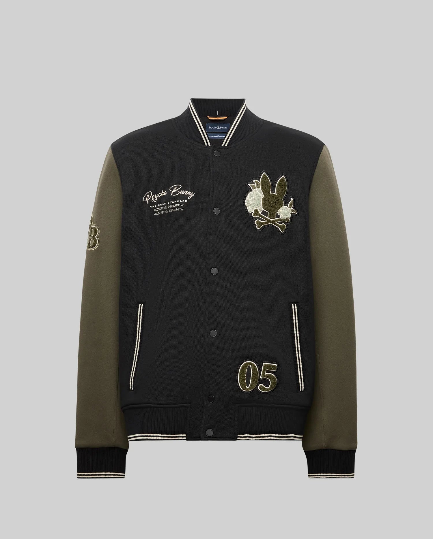 The Psycho Bunny MENS AUG﻿USTE KNIT BOMBER (MO1100050) is a black and olive varsity jacket with front snap buttons, embroidered text, chenille bunny and flower patches, number "05" on one side, and "53" on the sleeve; shown on a gray background.