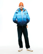 Men's Solan Puffer Jacket, a classic fit quilted puffer jacket featuring a blue ombre design from light to dark, with a vibrant orange interior lining and a small embroidered Psycho Bunny skull logo on the left chest. (6)
