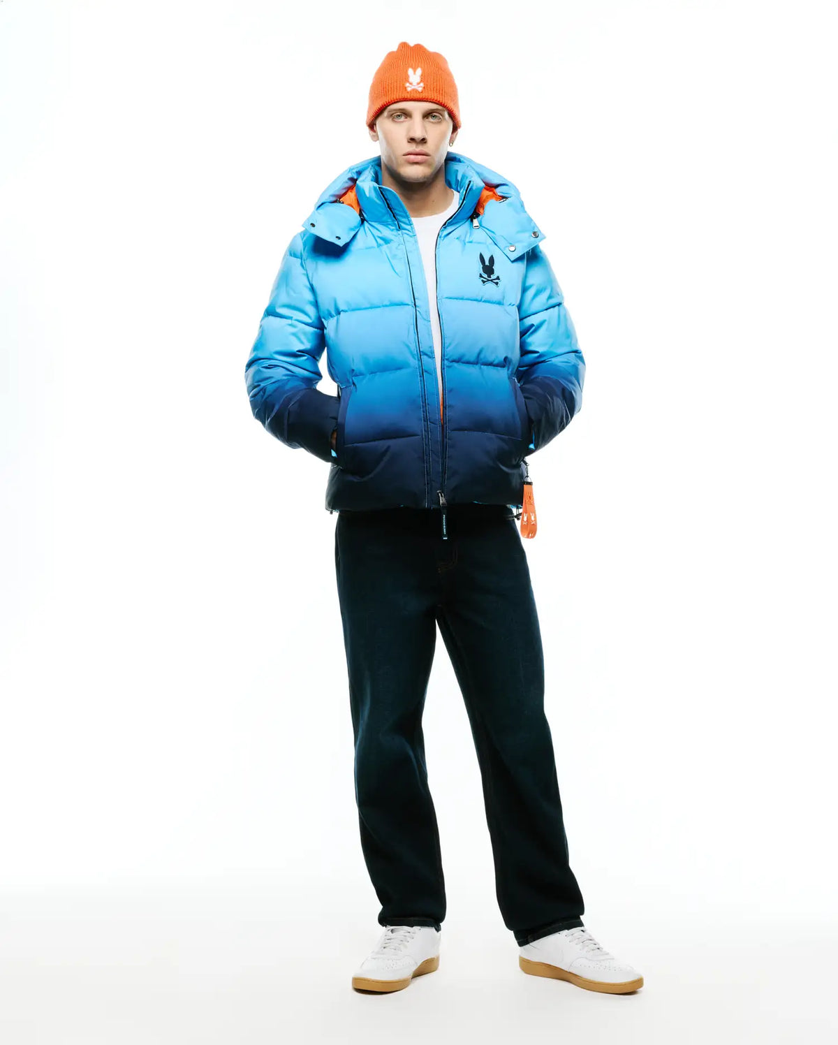Men's Solan Puffer Jacket, a classic fit quilted puffer jacket featuring a blue ombre design from light to dark, with a vibrant orange interior lining and a small embroidered Psycho Bunny skull logo on the left chest. (6)