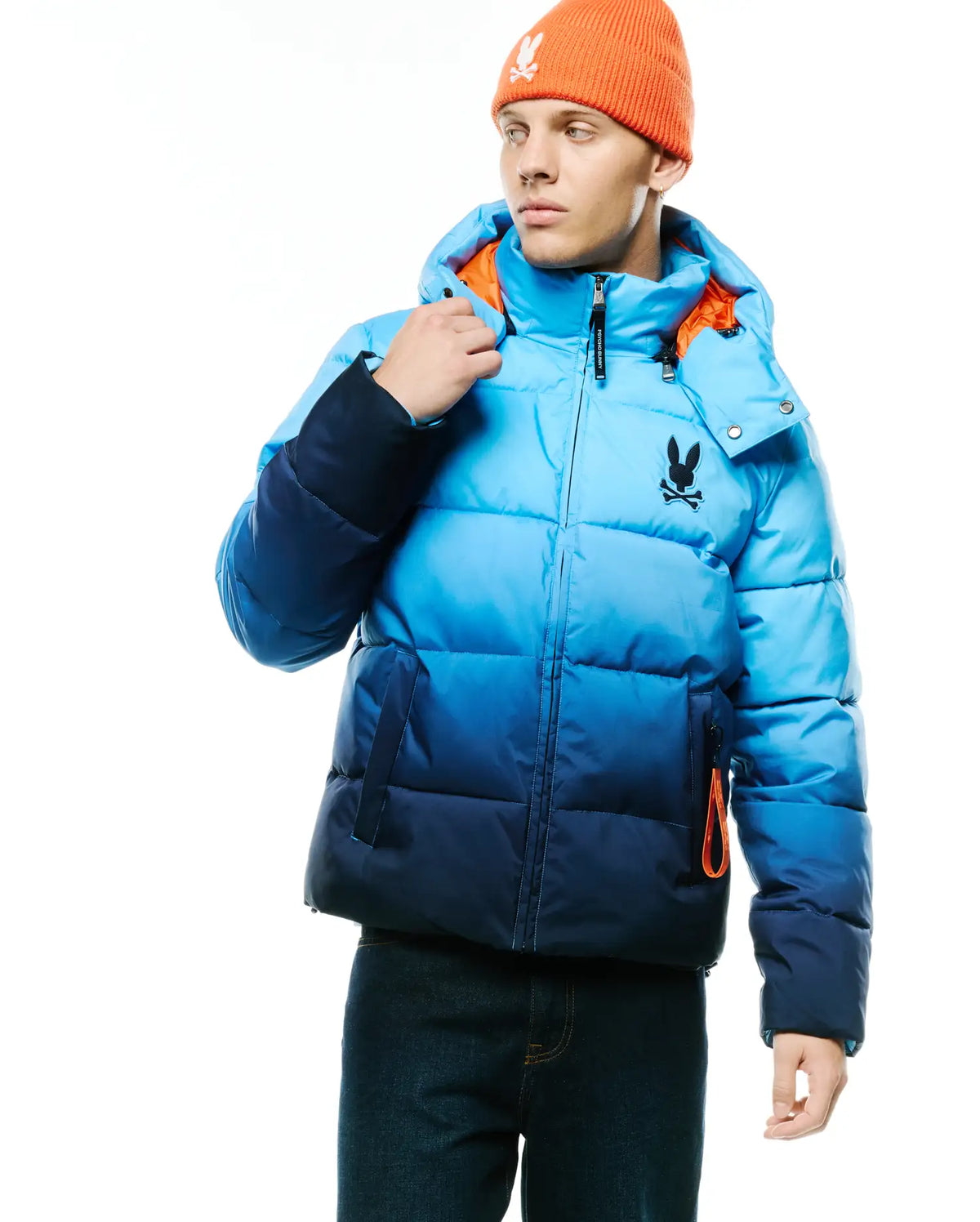 Men's Solan Puffer Jacket, an ombre blue quilted puffer jacket with a hooded design, featuring a black Psycho Bunny skull logo on the left chest and bright orange lining accents. (2)