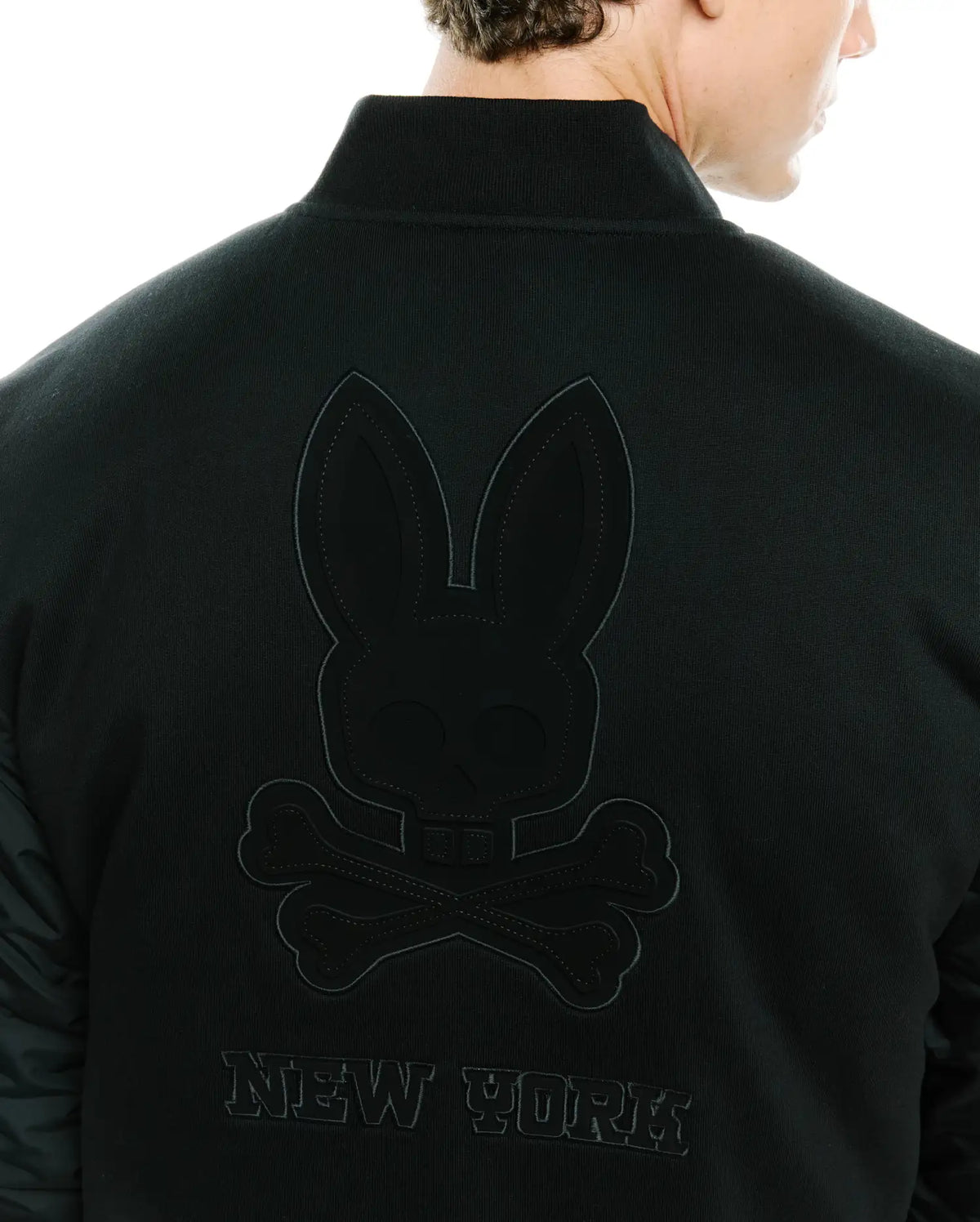 Mens Joaquin Mix Media Reversible Bomber in black, featuring a large tonal embroidered Psycho Bunny skull logo and NEW YORK text on the back, with contrasting quilted sleeves. (2)