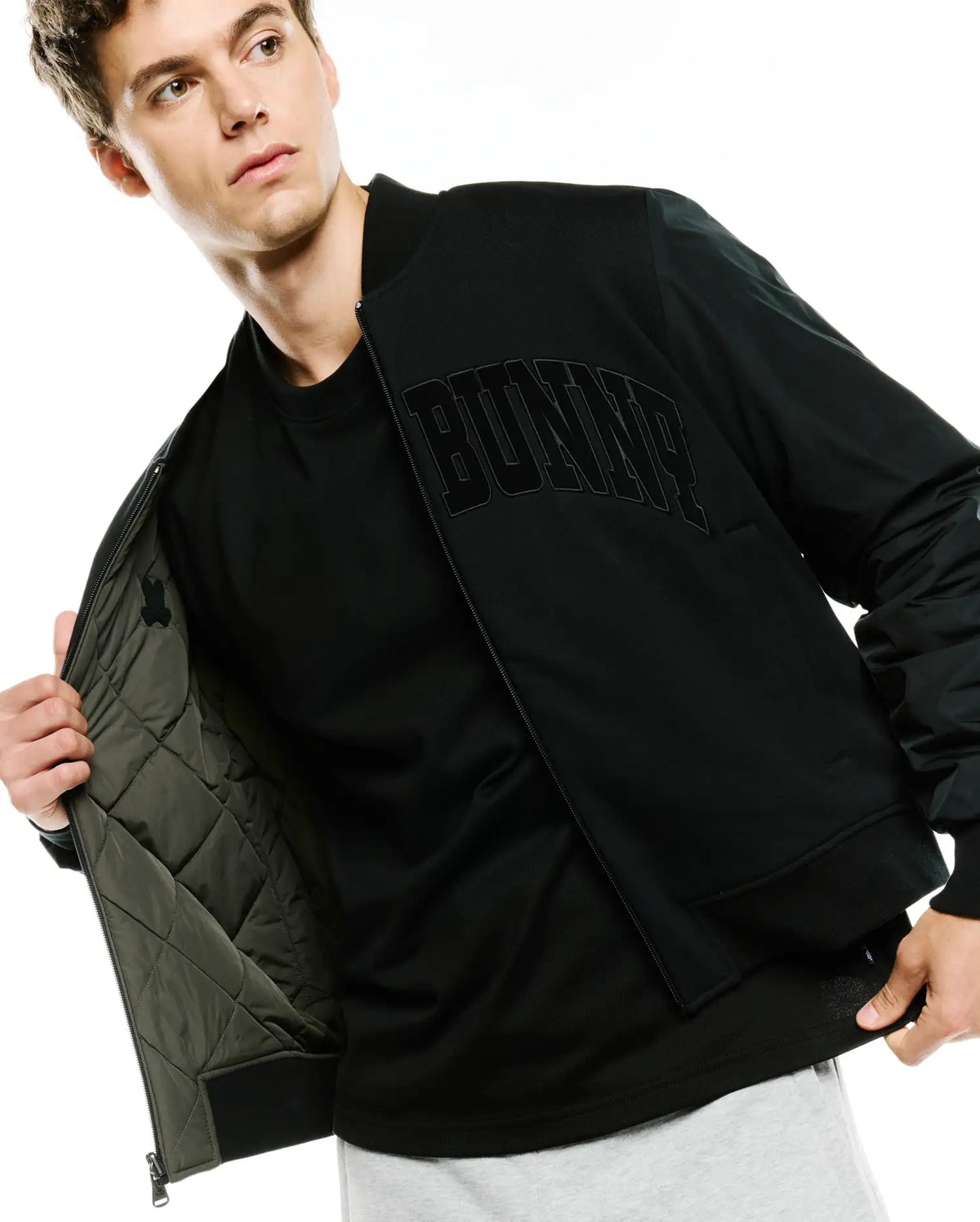 Black Mens Joaquin Mix Media Reversible Bomber jacket with large embroidered BUNNY text on chest, smooth outer fabric, and olive green quilted lining featuring a small Psycho Bunny skull logo. (6)