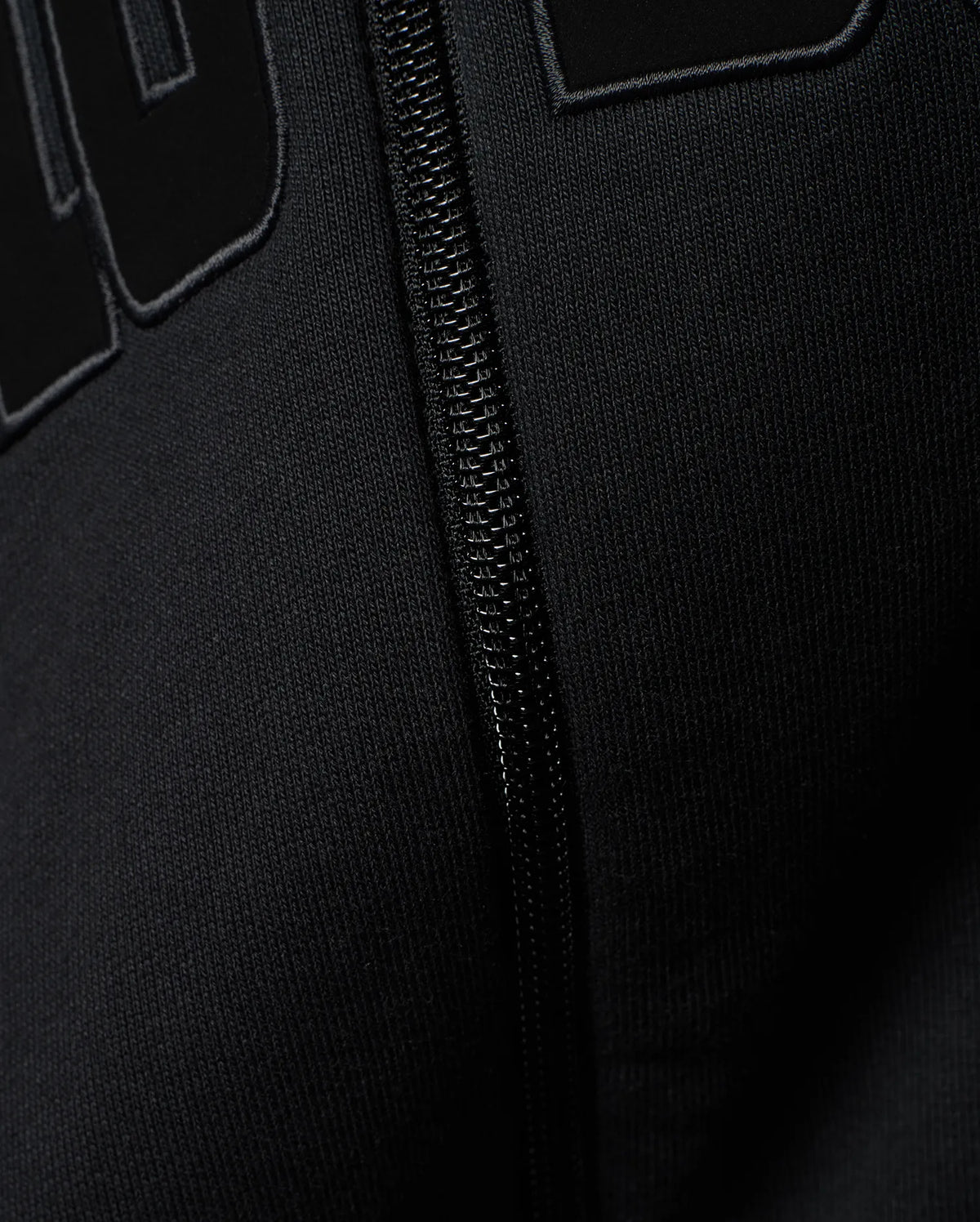 Mens Joaquin Mix Media Reversible Bomber in black, showcasing large raised black letters with a subtle grey outline on a smooth knit fabric, alongside a black front zipper. (3)
