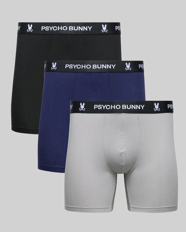 The Psycho Bunny MENS 3 PACK BOXER BRIEF (MO1400006) features three pairs in black, navy blue, and light gray with a black branded waistband and bunny logo, displayed against a plain gray background.