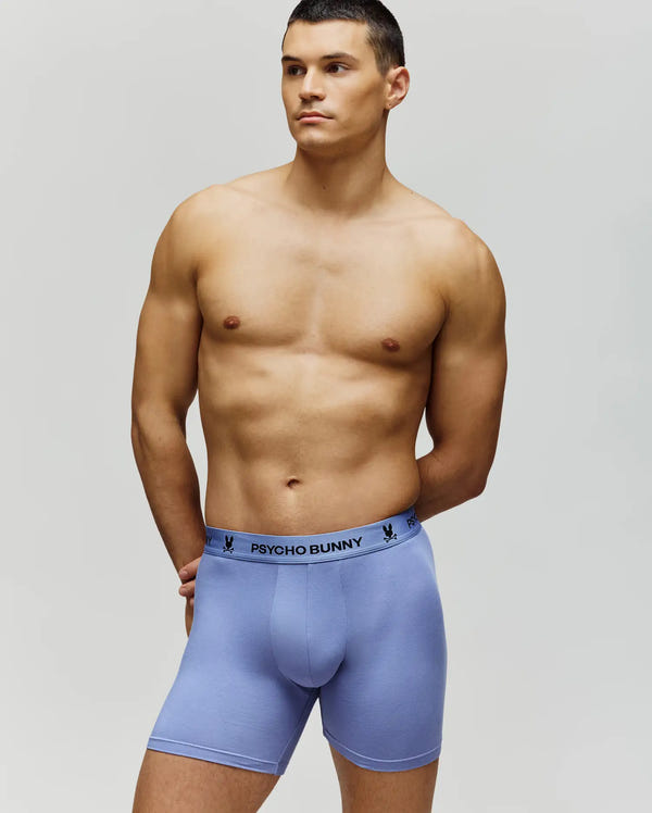 A shirtless man models Psycho Bunny's MENS 3 PACK BOXER BRIEF - MO1400008 in light purple, featuring a branded waistband, against a plain background, conveying all-day comfort.