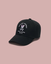 The Psycho Bunny MENS ARCHIVE BASEBALL CAP - MO1500002 is a black cotton cap with an embroidered Bunny and crossbones logo plus "Psycho Bunny Bold Since 2005" on the front. It features an adjustable strap and is shown on a plain pink background.