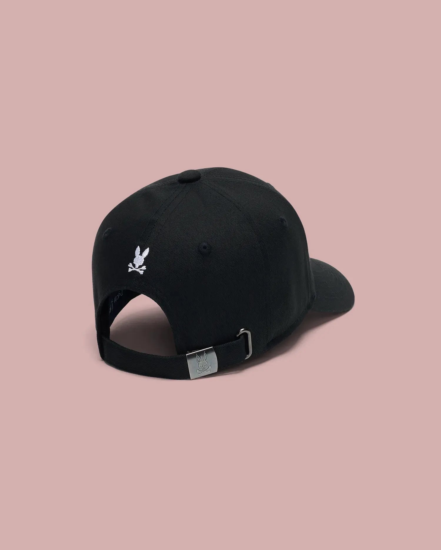 The MENS ARCHIVE BASEBALL CAP (MO1500002) by Psycho Bunny is shown from the back in black cotton, featuring a small white embroidered Bunny logo above its adjustable strap, set against a plain light pink background.