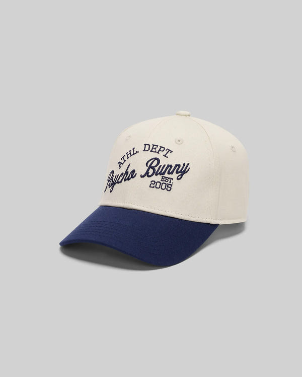 The Psycho Bunny MENS MATTEO BASEBALL CAP (MO1500008) features a two-tone Varsity style with a cream crown, navy blue brim, navy embroidered text on the front, and an adjustable strap for a perfect fit.