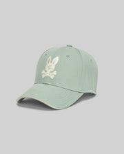 The Psycho Bunny MENS DEREK BASEBALL CAP - MO1500009 is a bold light green cotton cap with a white bunny skull and crossbones logo on the front, shown against a plain light gray background.