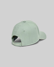 The MENS DEREK BASEBALL CAP - MO1500009 by Psycho Bunny is a light green premium cotton cap with an adjustable strap and bold "Psycho Bunny" embroidery, shown from the back against a plain grey background.