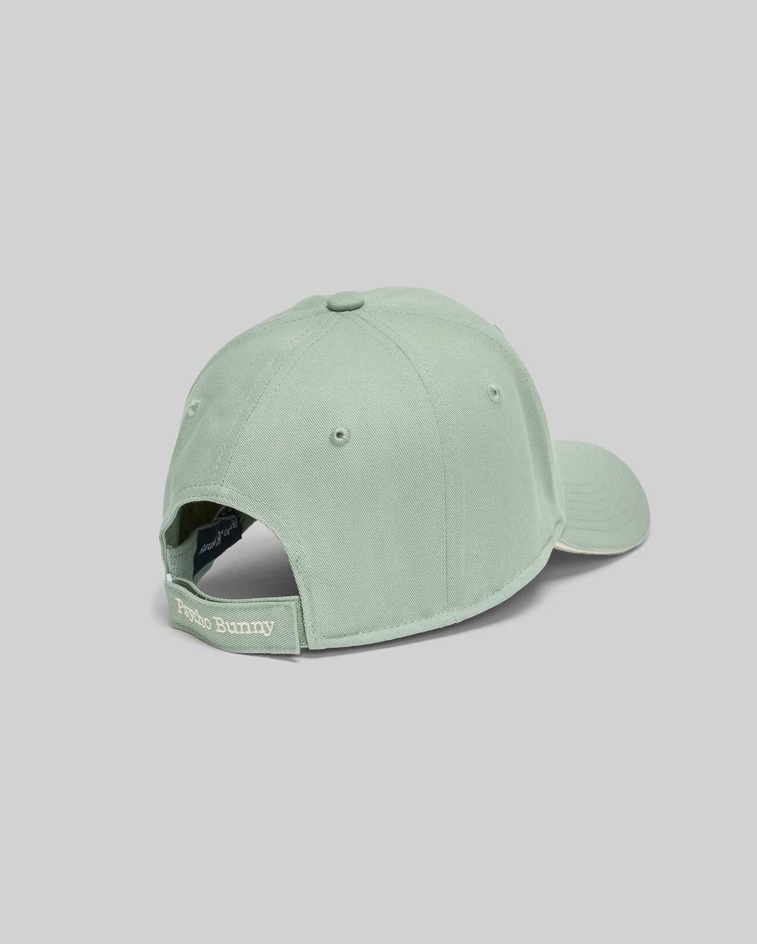 The MENS DEREK BASEBALL CAP - MO1500009 by Psycho Bunny is a light green premium cotton cap with an adjustable strap and bold "Psycho Bunny" embroidery, shown from the back against a plain grey background.