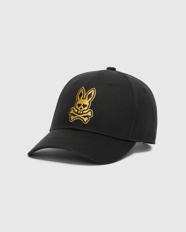 The Psycho Bunny MENS LAS VEGAS BASEBALL CAP (MO1500011) features a curved brim, 100% cotton construction, and gold direct embroidery of a bunny head above crossed bones. Made in China, it stands out against a light gray background.
