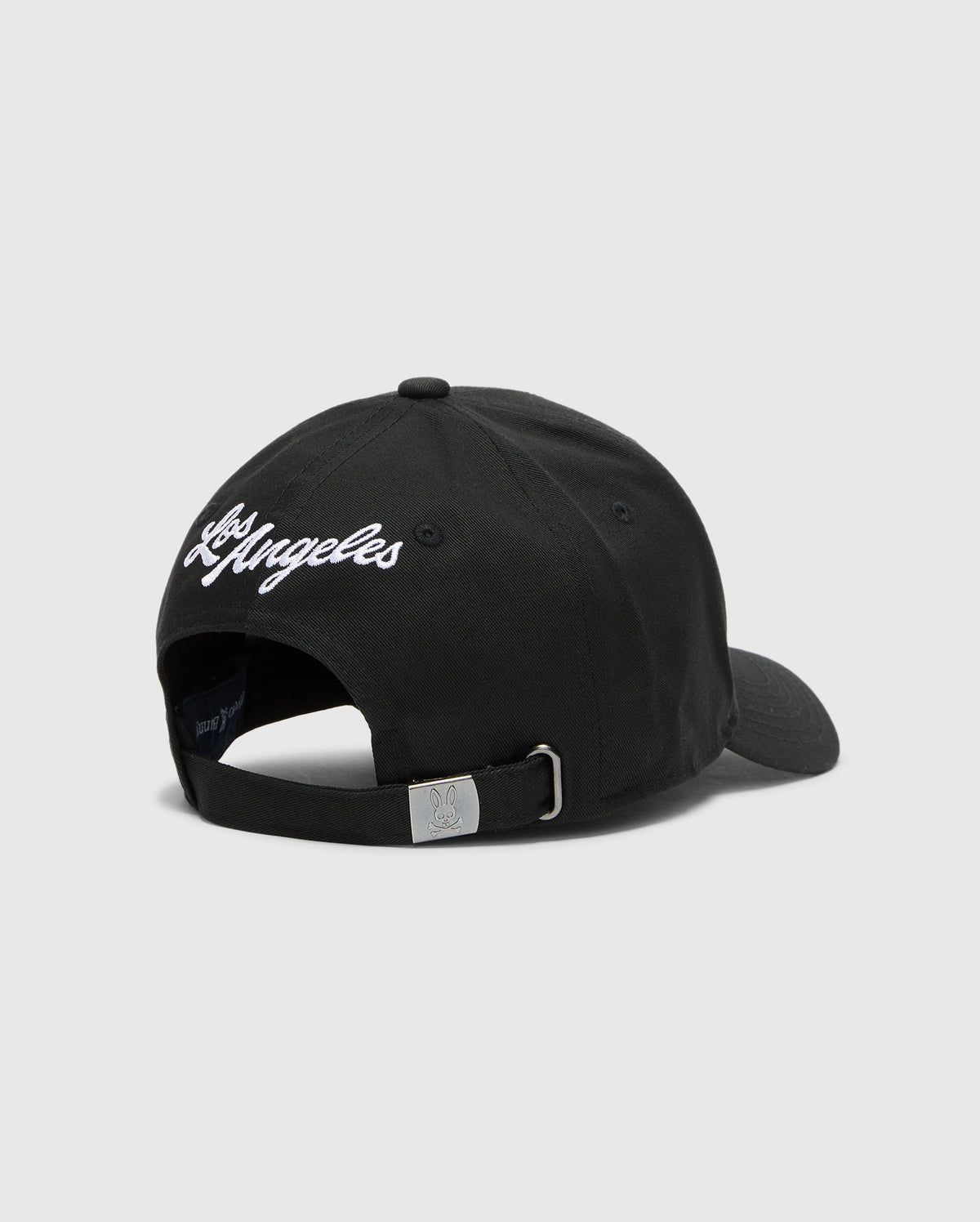The Psycho Bunny MENS LOS ANGELES BASEBALL CAP (MO1500013) is a black cotton cap featuring "Los Angeles" embroidered in white on the back, with an adjustable strap, metal buckle, and a small woven logo.