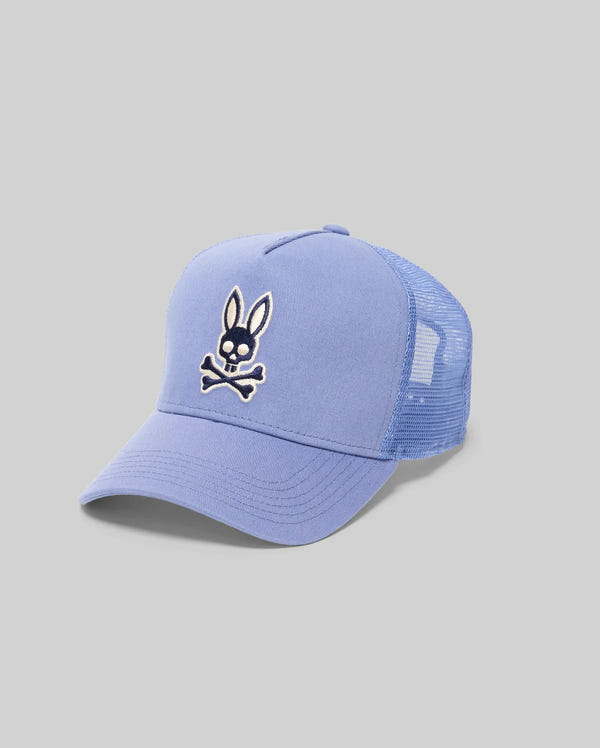 The Psycho Bunny MENS RYDER TRUCKER CAP (MO1500030) is a light blue cotton twill mesh cap with a curved brim, featuring an embroidered cartoon bunny above crossed bones and an adjustable snapback. Plain gray background.