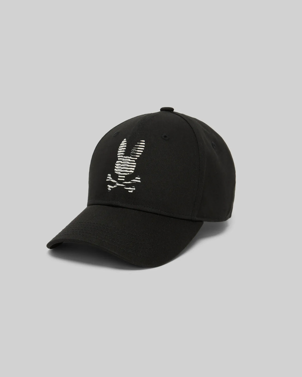 The Psycho Bunny MENS GRANT BASEBALL CAP (MO1500037) is a black cotton twill cap with an embroidered white skull and crossbones with rabbit ears on the front and an adjustable backstrap, shown on a plain gray background.