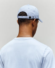 A person is seen from behind wearing a light blue T-shirt and the Psycho Bunny MENS GRANT BASEBALL CAP - MO1500﻿037, a cotton cap with an adjustable backstrap and white text on the back, set against a plain background.