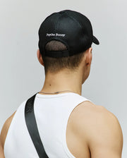A person, shown from the back against a light gray background, wears a white tank top and the Psycho Bunny MENS DARIO TRUCKER CAP (MO1500044), a black mesh breathable cap with "Psycho Bunny" text and adjustable snap-back.