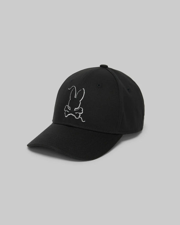 The Psycho Bunny MENS CYRUS BASEBALL CAP - MO1500045 is a black cap with a curved brim, featuring a white embroidered rabbit head and crossbones on the front. The background is plain light gray.