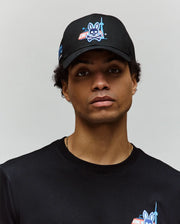 A man wears the Psycho Bunny MENS TORONTO BASEBALL CAP - MO1500049 and a matching tee, both with blue cartoon rabbit and CN Tower graphics, looking at the camera against a plain light background.