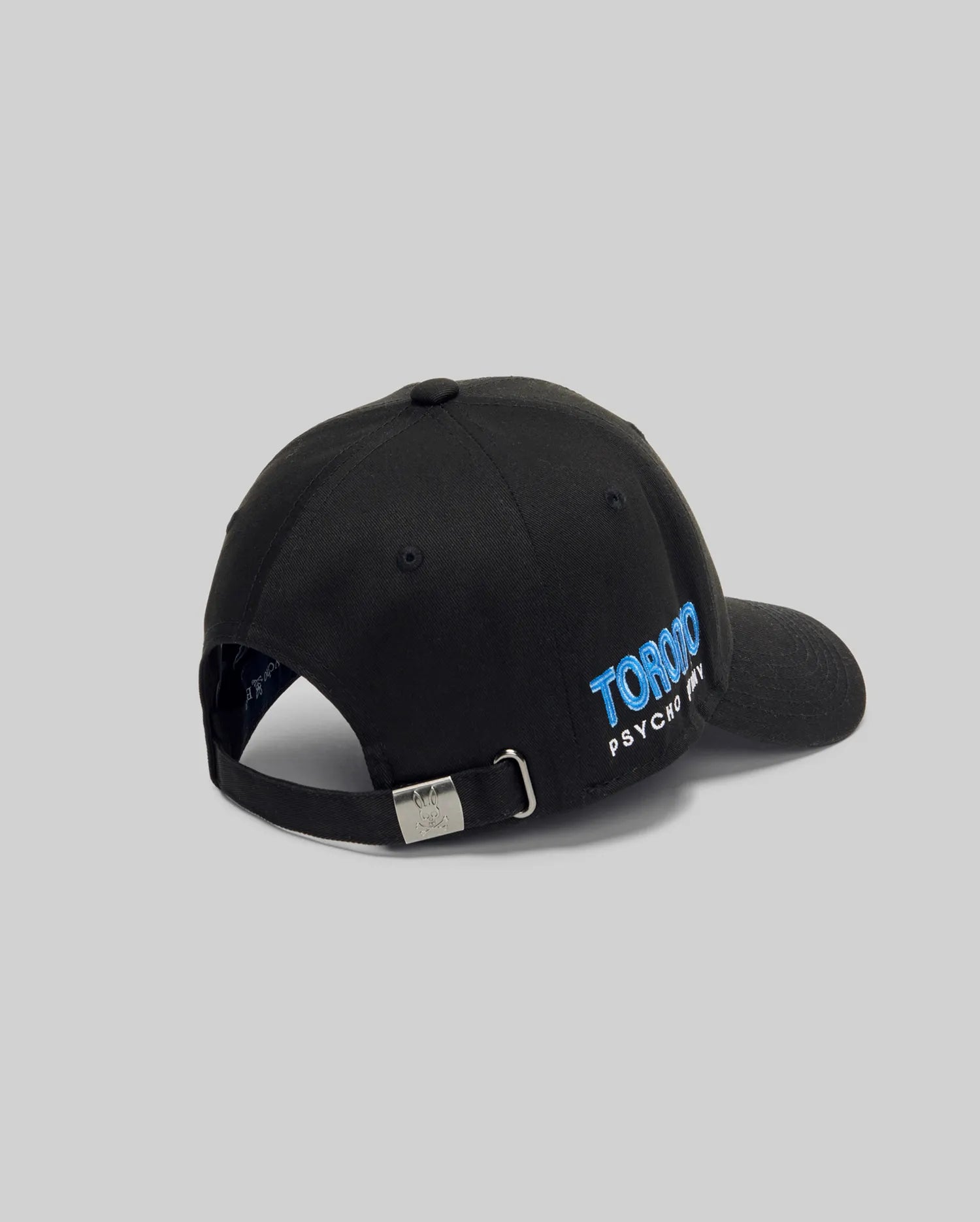 The Psycho Bunny MENS TORONTO BASEBALL CAP (MO1500049) is a black hat with an adjustable back strap, metal clasp, "TORONTO" embroidered in blue, and "PSYCHO" in white on the side. Plain gray background.