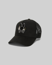 The Psycho Bunny MENS AUGUSTE TRUCKER CAP (MO1500050) is a black mesh-back hat with an embroidered cartoon bunny and crossbones chenille patch on the front. Features an adjustable snapback for comfort. Shown on a light gray background.
