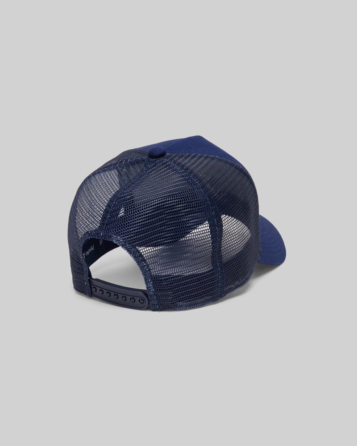 The Psycho Bunny MENS AUGUSTE TRUCKER CAP (MO1500050) is shown from the back in navy, featuring a mesh panel and adjustable snapback closure, set against a plain gray background.