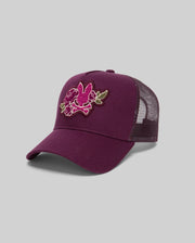 The Psycho Bunny MENS AUGUSTE TRUCKER CAP - MO1500050 is a maroon mesh hat with an embroidered pink and green floral front and adjustable snapback, shown against a plain gray background.