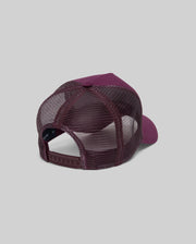 The Psycho Bunny MENS AUGUSTE TRUCKER CAP (MO1500050) is shown from the back in maroon, featuring mesh panels, a solid fabric front, and an adjustable snapback closure, set against a plain gray background.
