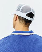 White Mens Adamo Trucker Cap with mesh back and snap closure, paired with a royal blue pique polo shirt featuring a blue and white striped collar. (3)