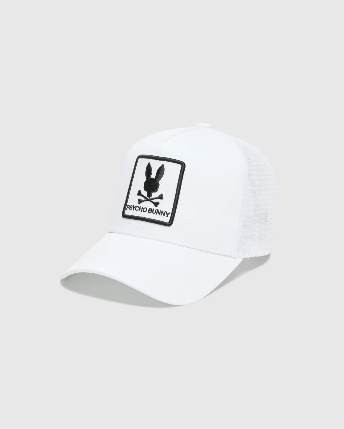White Mens Adamo Trucker Cap featuring a large, centered black embroidered Psycho Bunny skull and crossbones logo patch with PSYCHO BUNNY text on the solid front panel and a breathable mesh back. (2)