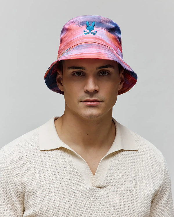 Mens Raphael Bucket Hat in a vibrant multi-color swirl pattern with an embroidered blue Psycho Bunny logo, paired with a cream textured knit polo featuring a small embroidered Psycho Bunny logo.