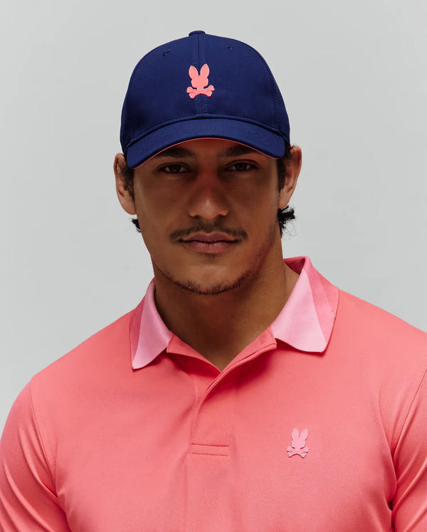 Mens Onyx Sport Cap in navy with pink Psycho Bunny skull logo and brim trim, paired with a coral pique polo shirt featuring a lighter pink collar and matching embroidered Psycho Bunny skull.
