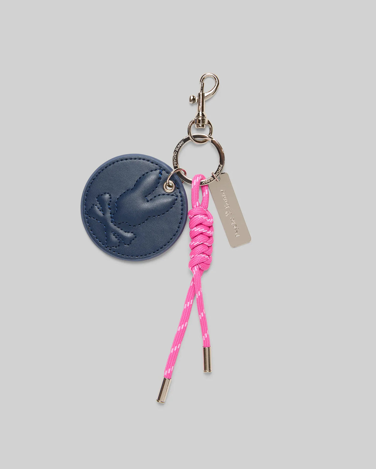 The Psycho Bunny DISC KEYCHAIN - MO1700013 features a round blue faux-leather tag embossed with a bird, a pink knotted cord with metal tips, and a small metal tag, all attached to a sturdy lanyard clasp.