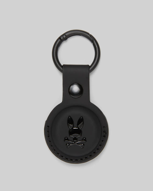 The Psycho Bunny MENS AIR TAG HOLDER - MO1700017 is a round, black leather holder with an embossed bunny logo, snap button, and metal keyring—ideal as a stylish luggage tag.