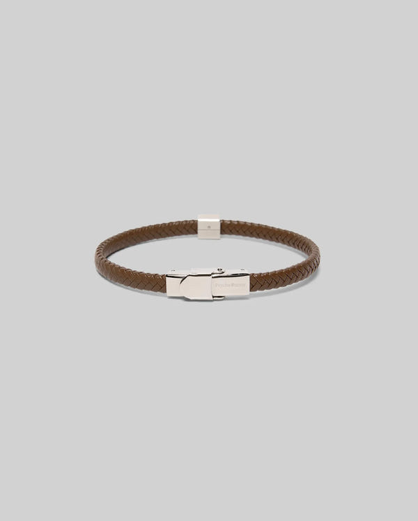The Psycho Bunny MENS LEATHER BRAIDED BRACELET (MO1700020) features brown braided leather and a sleek silver hinged clasp, shown on a plain light gray background.