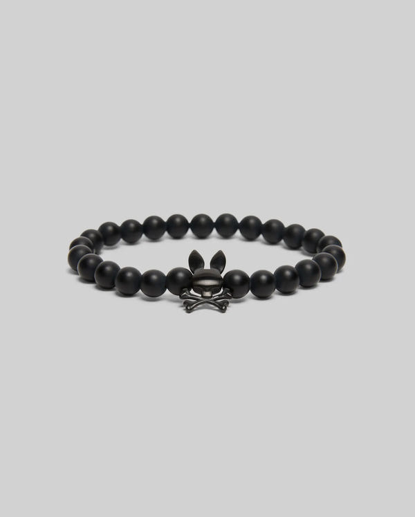 The Psycho Bunny MENS BUNNY BEAD BRACELET (MO1700023) features black beads and a metallic skull-and-crossbones charm with bunny ears—ideal as a subtle fidget or stylish accent—shown on a simple light gray background.