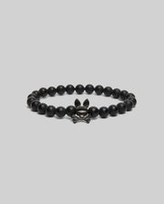 The Psycho Bunny MENS BUNNY BEAD BRACELET (MO1700023) features black beads and a metallic skull-and-crossbones charm with bunny ears—ideal as a subtle fidget or stylish accent—shown on a simple light gray background.