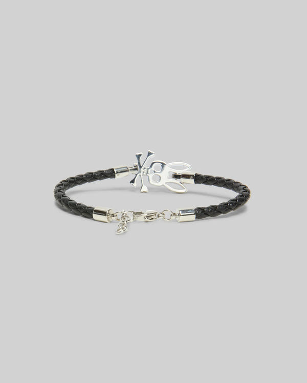 The Psycho Bunny MENS BUNNY LEATHER BRACELET (MO1700024) features black braided leather with a silver skull and crossbones charm and metal clasp, ideal for daily wear, shown on a plain light gray background.