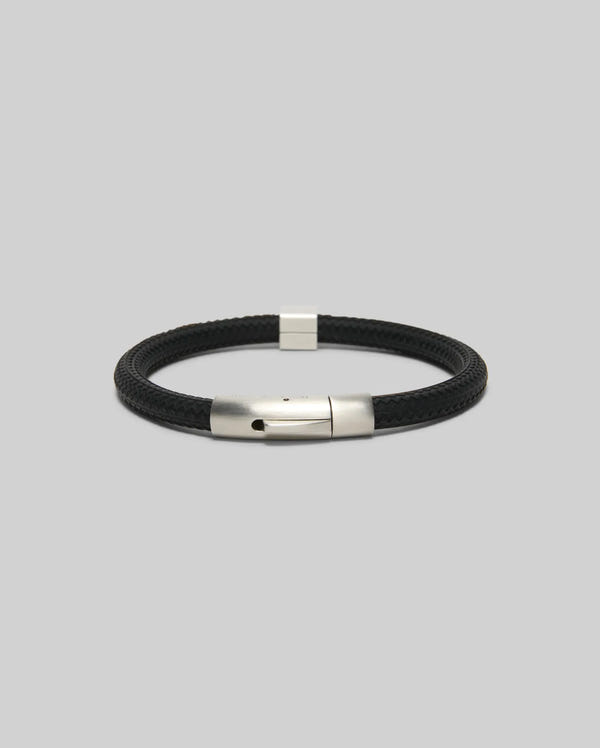 The Psycho Bunny MENS SILICONE BRACELET - MO1700025 features a black braided design with a sleek silver metal clasp, showcased on a plain light gray background.