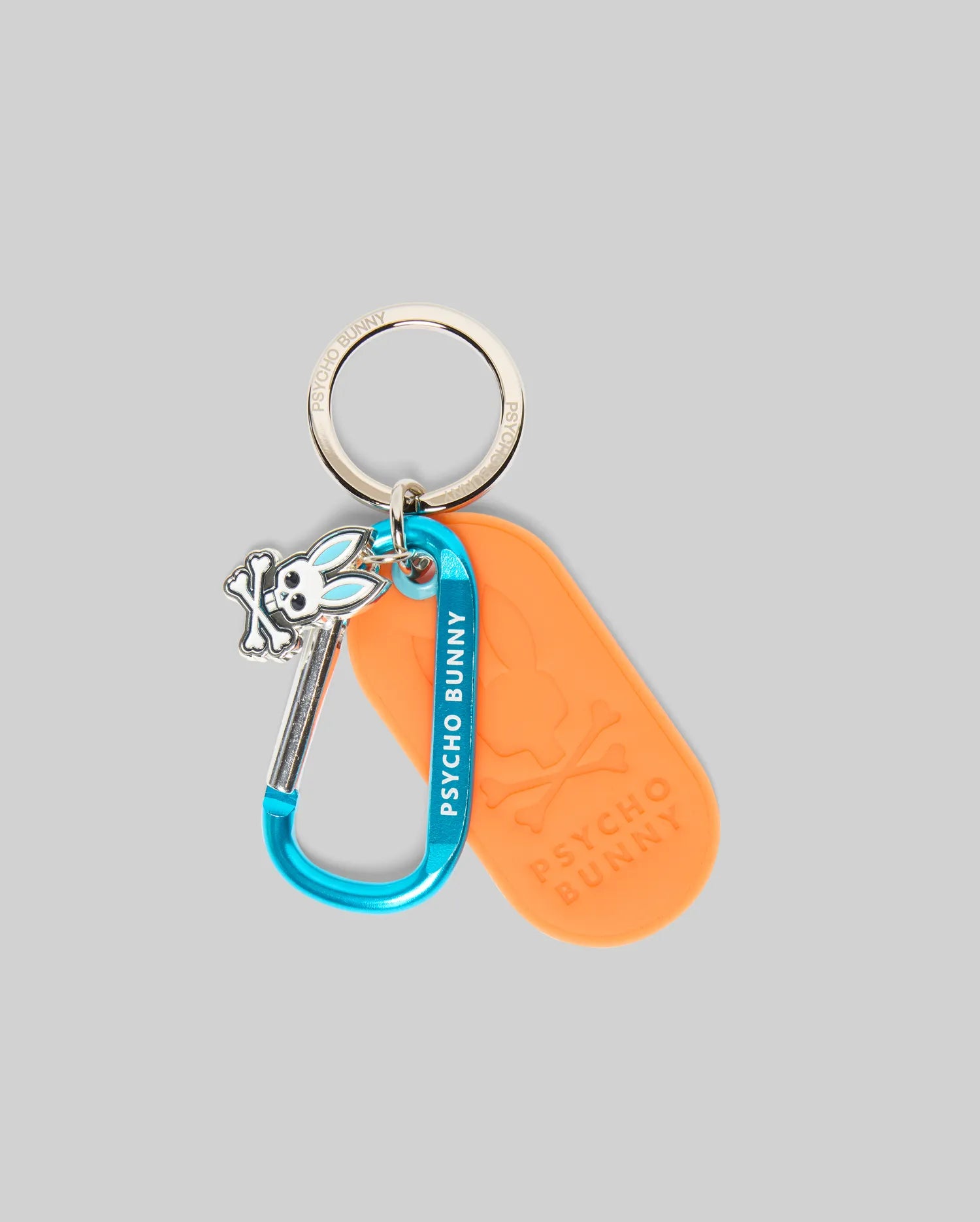 Mens Carabiner Keychain featuring a silver ring engraved with Psycho Bunny, a bright blue carabiner with white Psycho Bunny text, an orange embossed Psycho Bunny skull tag, and a small blue-accented bunny skull charm.