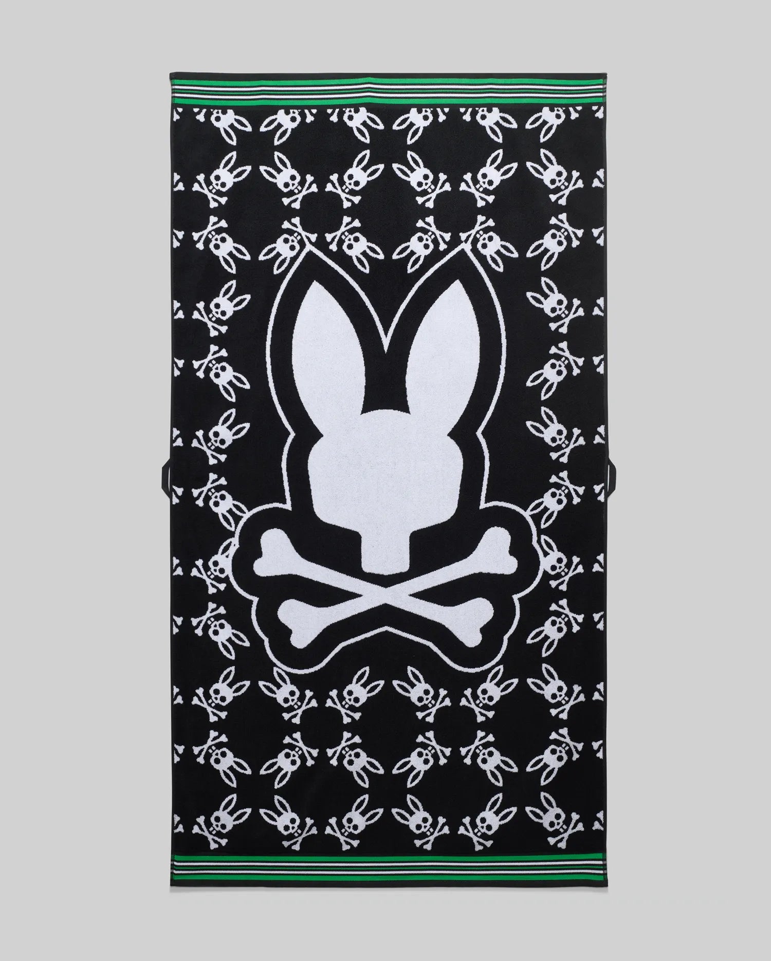 Mens All Over Bunny Towel in black terry cloth, featuring a large white central Psycho Bunny skull logo and an all-over pattern of smaller white bunny skulls, finished with green and white striped borders.