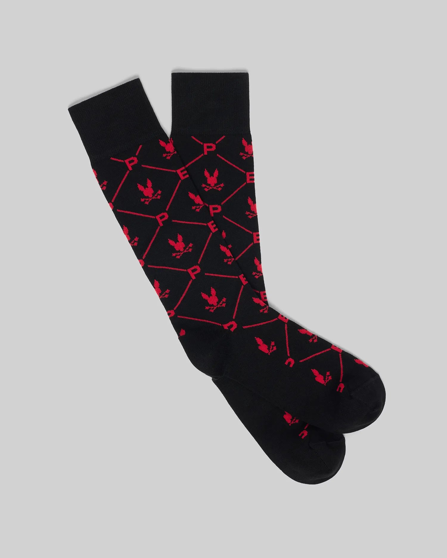The Psycho Bunny MENS 2 PACK DRESS SOCK - MO2200005 features black knee-high socks with a red hexagonal pattern, "P" designs, and small eagle icons, shown on a light gray background.